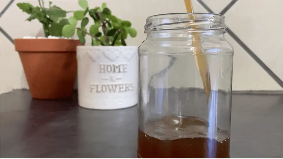 Honey syrup being poured into a mason jar in front of plants.