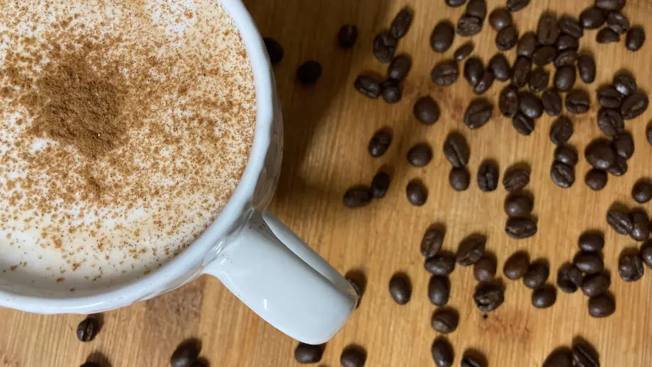Cinnamon Dolce Latte and coffee beans on wooden surface.