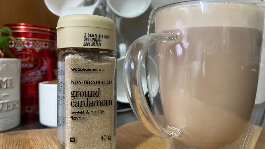 Cardamom coffee in a double walled mug next to ground cardamom.