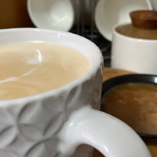Caramel Latte in white textured mug with caramel sauce in black bowl.