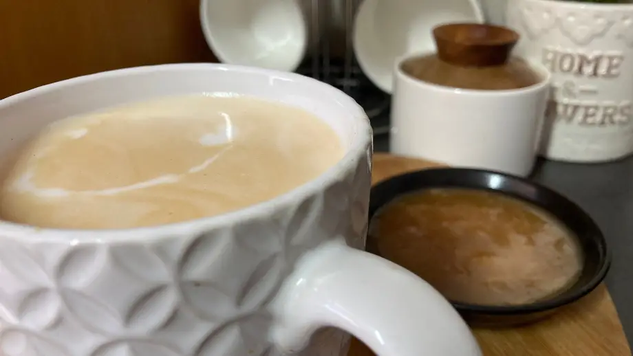 Caramel Latte in white textured mug with caramel sauce in black bowl.