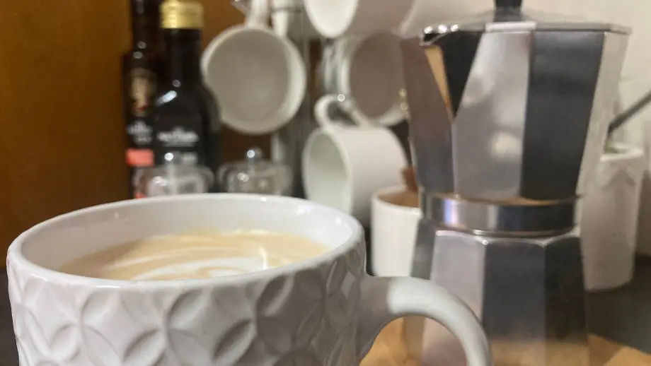Latte in white textured mug in front of a Moka pot.