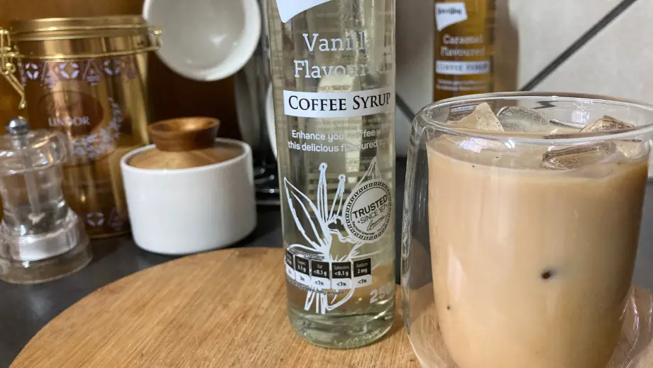 Vanilla iced coffee next to vanilla syrup.